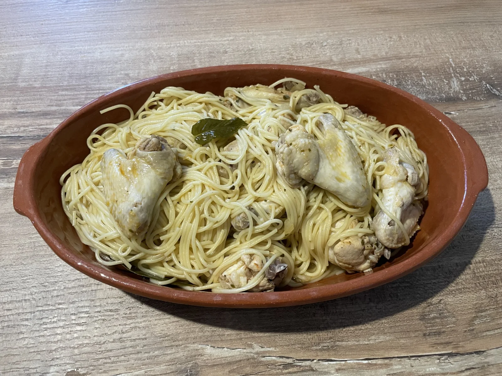 Ailes de poulet aux spaghettis servies dans un plat en terre cuite